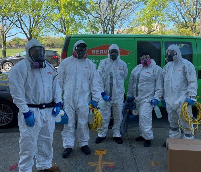 SERVPRO team members, donned in PPE, standing in front of SERVPRO van